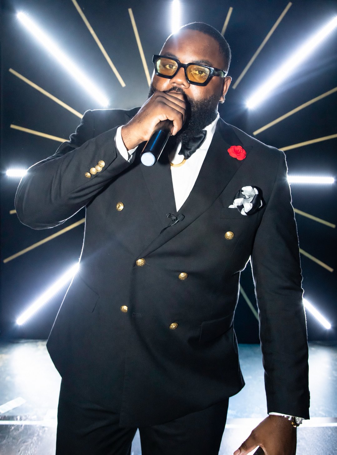 Alex Ikemefuna Ozoh II on the mic in a black double-breasted suit